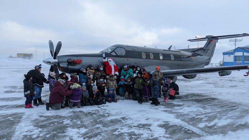 Santa surrounded by Inuit children in front of Arctic Fresh Group flight with hamper donations